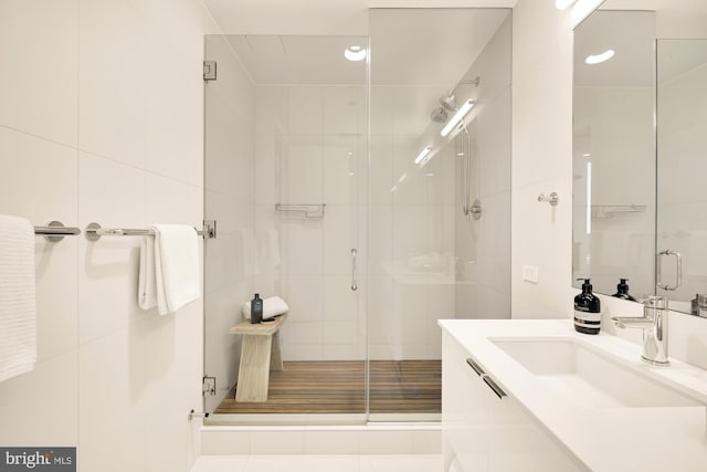 bathroom with vanity, a shower with shower door, and tile walls