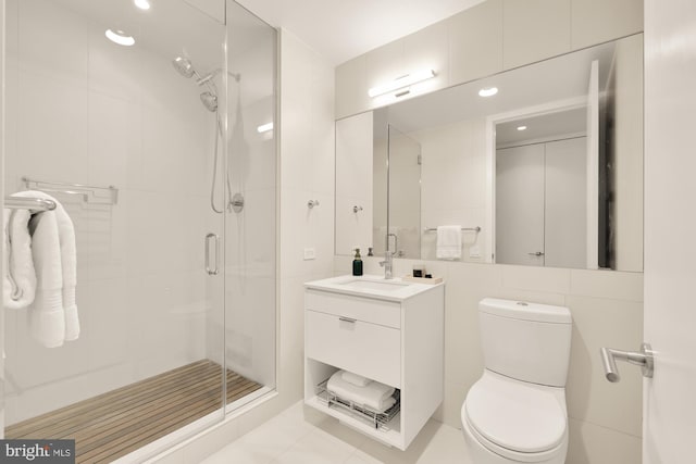 bathroom featuring tile patterned floors, toilet, vanity, a shower with shower door, and tile walls