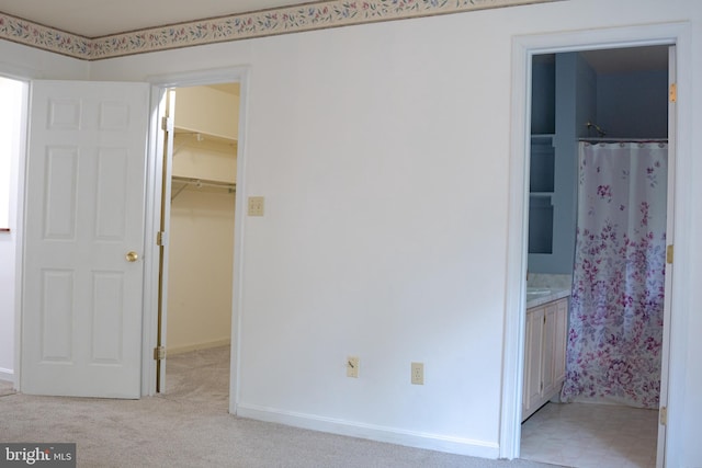 unfurnished bedroom featuring light carpet, a closet, connected bathroom, and a walk in closet