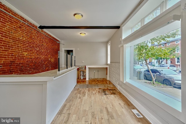 corridor with light hardwood / wood-style floors, brick wall, and crown molding