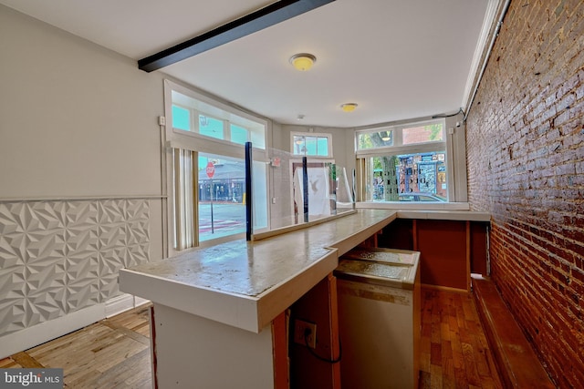 kitchen with light hardwood / wood-style flooring, beam ceiling, kitchen peninsula, and brick wall