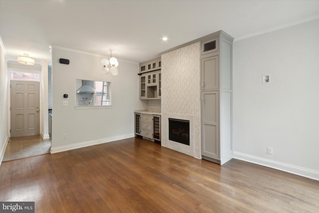 unfurnished living room featuring a fireplace, dark hardwood / wood-style flooring, crown molding, beverage cooler, and a notable chandelier