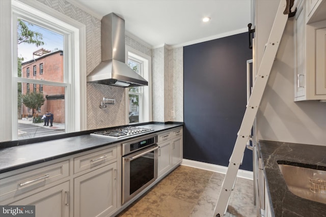 kitchen with ornamental molding, sink, wall chimney exhaust hood, stainless steel appliances, and a barn door