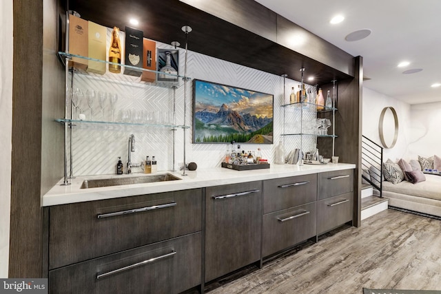 bar featuring dark brown cabinetry, decorative light fixtures, light hardwood / wood-style floors, and sink