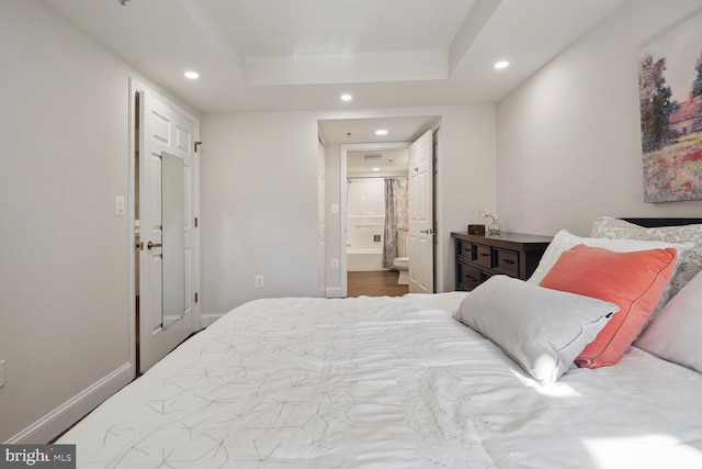 bedroom featuring wood-type flooring, a tray ceiling, and ensuite bathroom