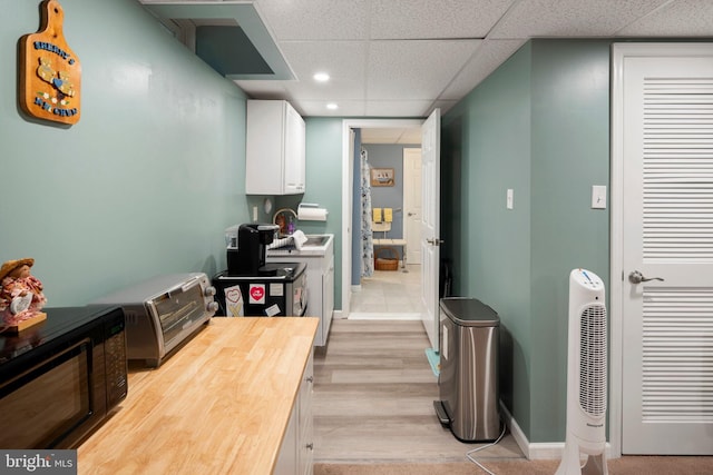 kitchen featuring light wood-type flooring, white cabinetry, a paneled ceiling, and wood counters