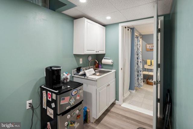 kitchen with white cabinetry, light hardwood / wood-style floors, sink, and a drop ceiling