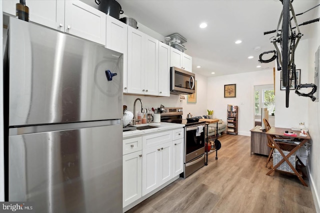 kitchen with light countertops, a sink, light wood finished floors, stainless steel appliances, and white cabinets