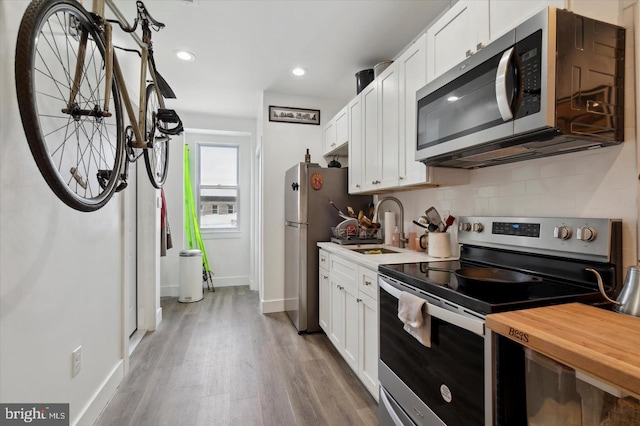 kitchen with wood counters, sink, white cabinets, light hardwood / wood-style flooring, and stainless steel appliances