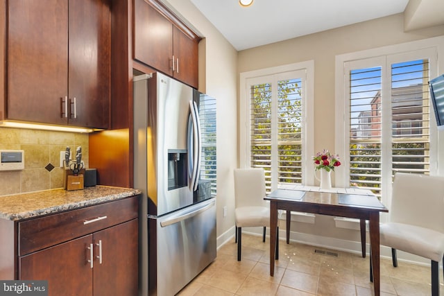 kitchen featuring light tile patterned flooring, light stone countertops, backsplash, and stainless steel fridge with ice dispenser