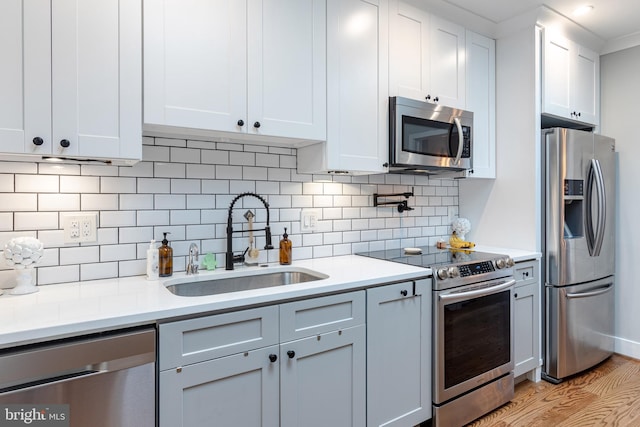 kitchen featuring tasteful backsplash, white cabinetry, appliances with stainless steel finishes, sink, and light hardwood / wood-style flooring