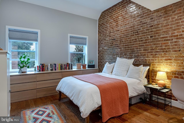 bedroom with dark wood-type flooring, multiple windows, brick wall, and vaulted ceiling