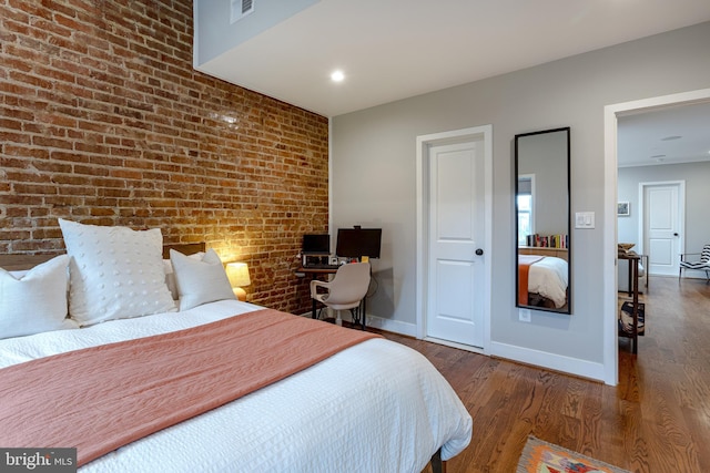 bedroom featuring dark wood-type flooring and brick wall