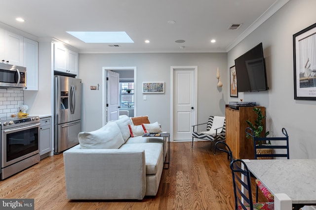 living room with light hardwood / wood-style floors, a skylight, and ornamental molding