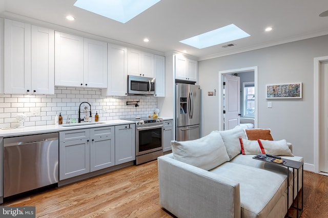 kitchen featuring ornamental molding, stainless steel appliances, sink, light hardwood / wood-style floors, and white cabinets