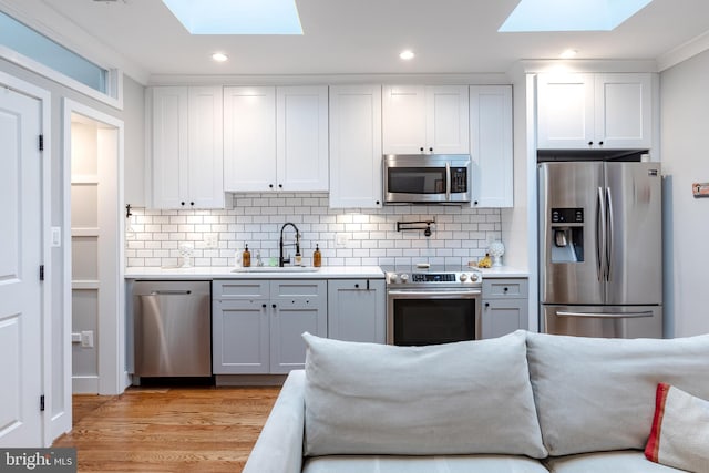 kitchen with appliances with stainless steel finishes, sink, light hardwood / wood-style floors, and white cabinets