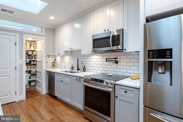 kitchen with stainless steel appliances, light hardwood / wood-style floors, sink, backsplash, and white cabinets