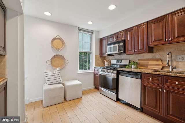 kitchen featuring sink, decorative backsplash, stainless steel appliances, light hardwood / wood-style flooring, and light stone countertops