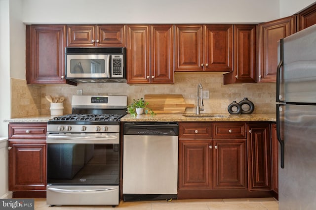 kitchen featuring light stone counters, tasteful backsplash, light tile patterned floors, stainless steel appliances, and sink