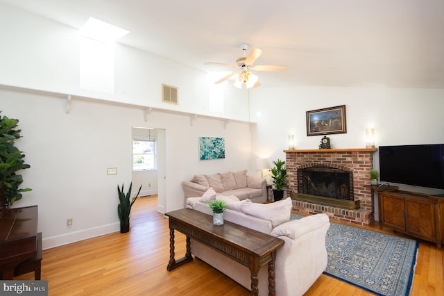 living room with light hardwood / wood-style floors, a fireplace, lofted ceiling with skylight, and ceiling fan