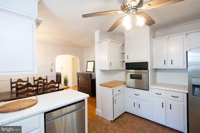 kitchen featuring white cabinetry, ceiling fan, stainless steel appliances, tile counters, and ornamental molding