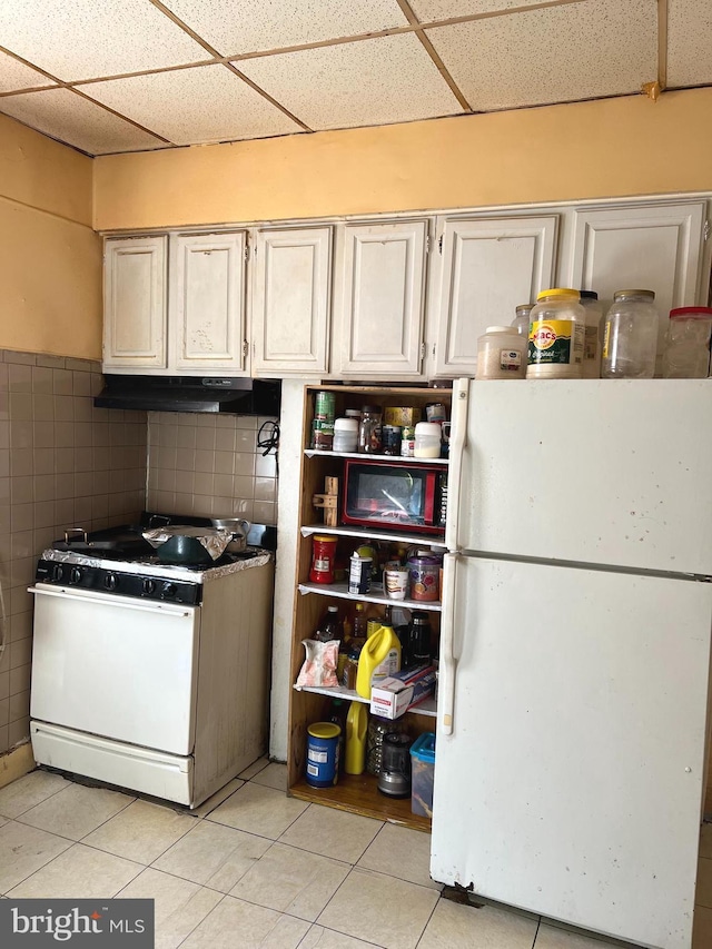 interior space with tile walls, a drop ceiling, light tile patterned floors, and white appliances