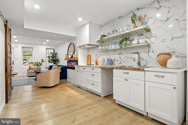 kitchen featuring sink, white cabinets, a barn door, light hardwood / wood-style flooring, and backsplash