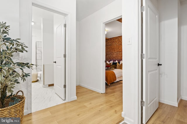 hallway with brick wall and light hardwood / wood-style floors