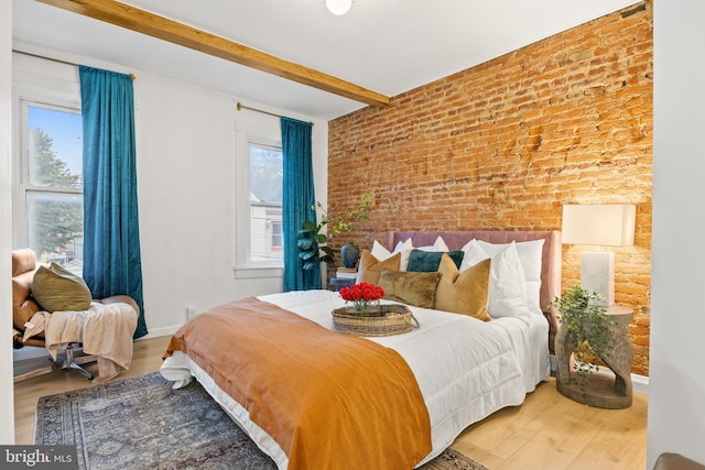 bedroom featuring wood-type flooring, beam ceiling, and brick wall