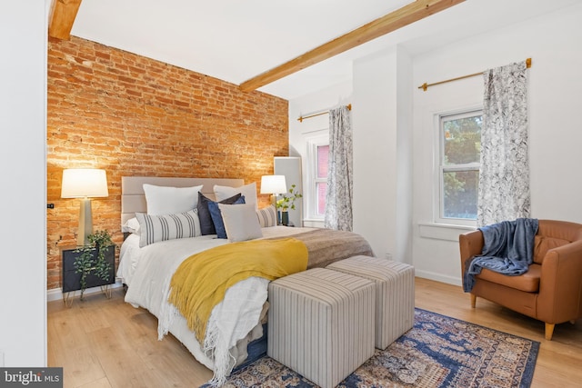 bedroom with brick wall, beamed ceiling, and light wood-type flooring