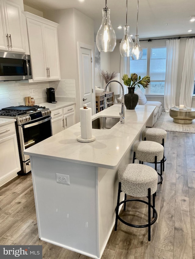 kitchen with appliances with stainless steel finishes, light hardwood / wood-style floors, an island with sink, white cabinets, and sink