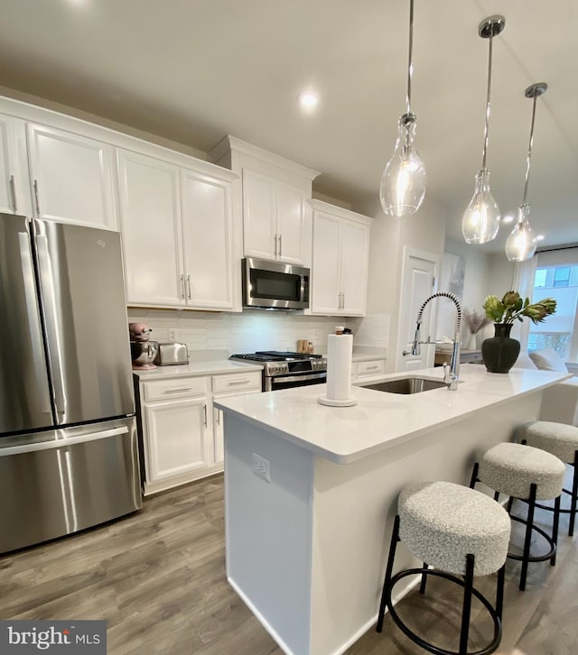 kitchen with an island with sink, white cabinetry, stainless steel appliances, and decorative light fixtures