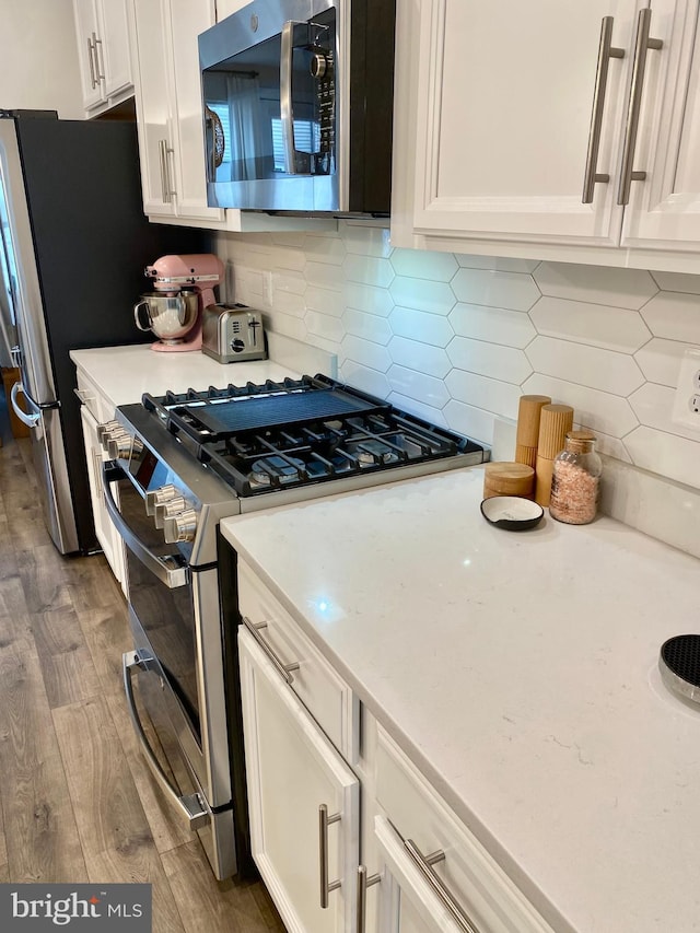 kitchen featuring stainless steel appliances, hardwood / wood-style floors, tasteful backsplash, and white cabinetry