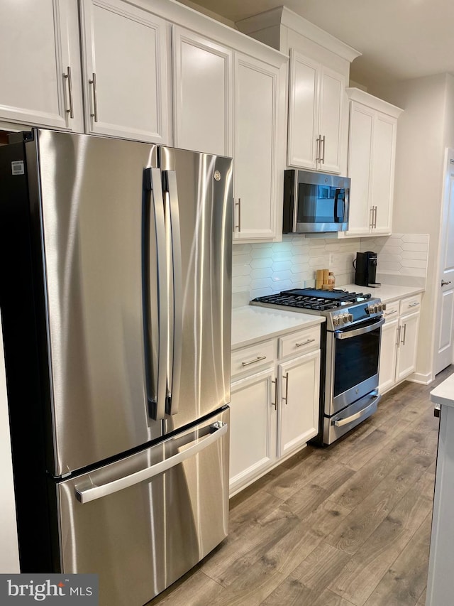 kitchen with light wood-type flooring, white cabinetry, appliances with stainless steel finishes, and backsplash