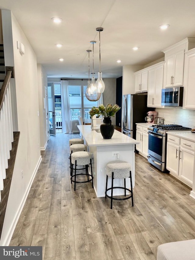 kitchen with decorative light fixtures, a center island with sink, appliances with stainless steel finishes, and white cabinets