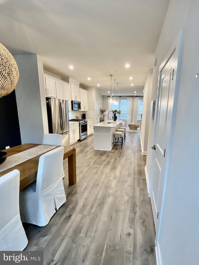 kitchen featuring an island with sink, white cabinets, light hardwood / wood-style flooring, stainless steel appliances, and decorative light fixtures