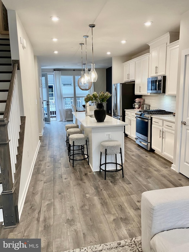 kitchen with appliances with stainless steel finishes, a kitchen island with sink, white cabinetry, and light hardwood / wood-style flooring