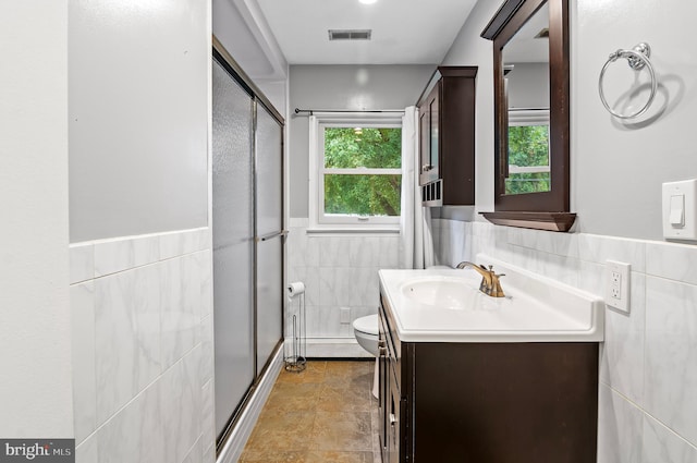 bathroom with tile walls, a shower with door, vanity, and toilet