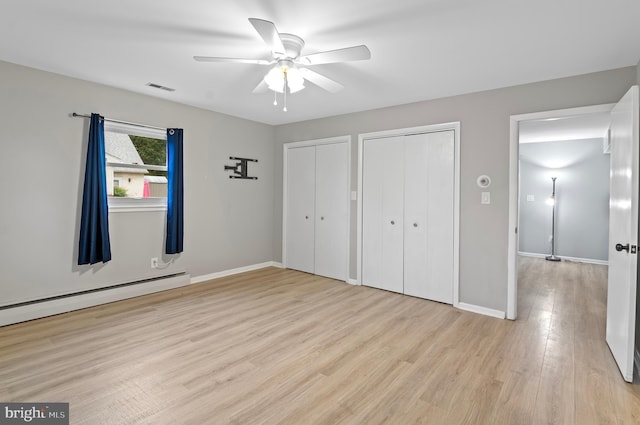 unfurnished bedroom featuring baseboard heating, two closets, ceiling fan, and light hardwood / wood-style flooring