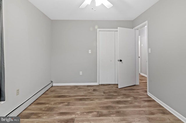 unfurnished bedroom with wood-type flooring, baseboard heating, ceiling fan, and a closet