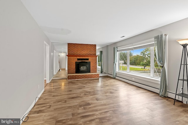 unfurnished living room with wood-type flooring, a baseboard heating unit, and a brick fireplace