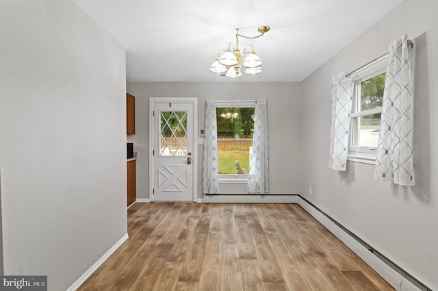 doorway to outside with a notable chandelier, light wood-type flooring, a baseboard heating unit, and a healthy amount of sunlight