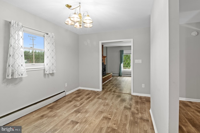 unfurnished room with wood-type flooring, an inviting chandelier, a brick fireplace, and a baseboard heating unit