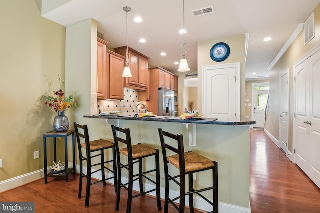 kitchen featuring pendant lighting, kitchen peninsula, dark wood-type flooring, stainless steel refrigerator with ice dispenser, and crown molding