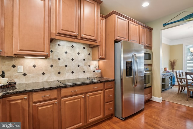 kitchen with light hardwood / wood-style floors, tasteful backsplash, crown molding, dark stone countertops, and stainless steel appliances