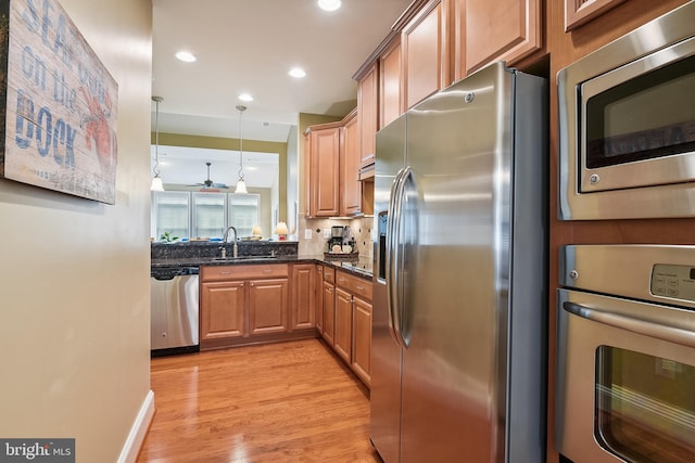 kitchen with ceiling fan, dark stone counters, light hardwood / wood-style flooring, decorative light fixtures, and appliances with stainless steel finishes