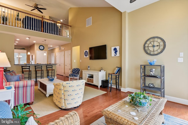 living room with hardwood / wood-style flooring, ceiling fan with notable chandelier, a fireplace, and high vaulted ceiling