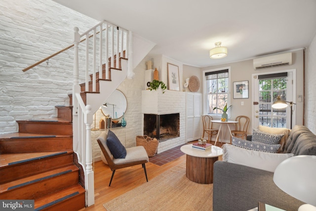 living room featuring a brick fireplace, hardwood / wood-style flooring, and a wall unit AC