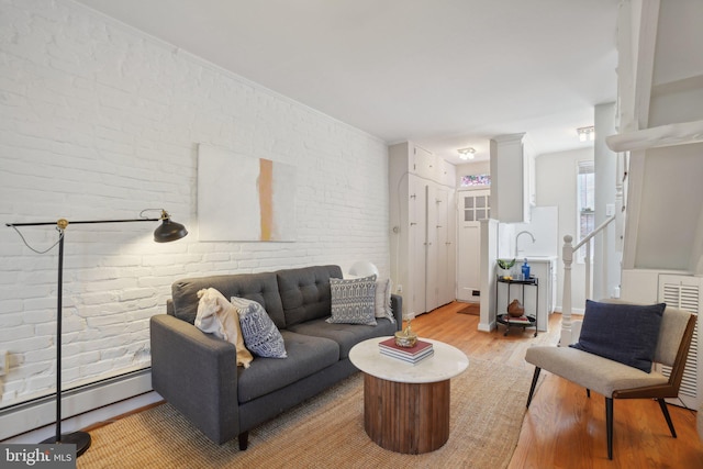 living room featuring brick wall, light wood-type flooring, and baseboard heating