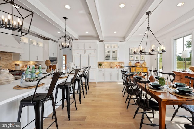 dining space with beamed ceiling, a notable chandelier, and light wood-type flooring